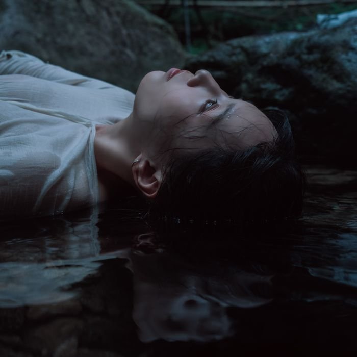 Moody portrait of a woman reflecting by water, capturing tranquility and introspection.